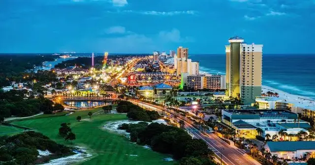 Evening skyline of Panama City, Florida with high-rise buildings, lit streets, and the Gulf beyond.