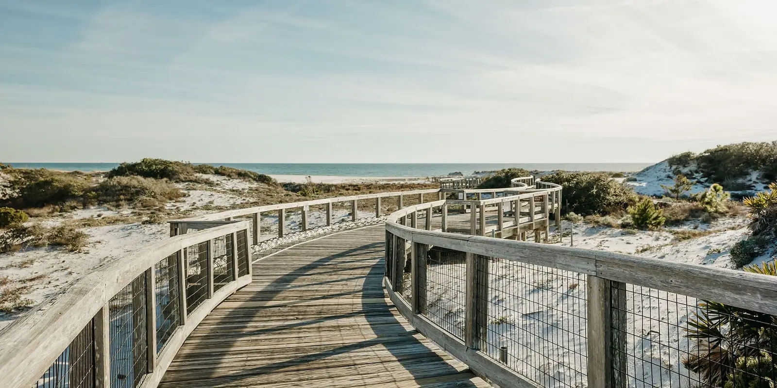 Weathered wooden boardwalk curving through white sand dunes toward the Gulf at WaterSound, Florida.