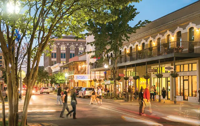Lively downtown street at dusk near Pace, Florida with lit storefronts, balconies, and pedestrians.