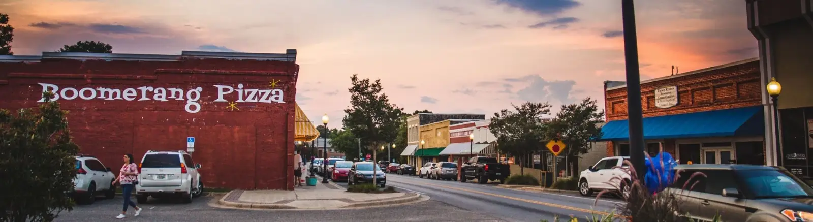 Downtown Milton, Florida at sunset — historic red-brick storefronts along Caroline Street with parked cars and warm pink sky.